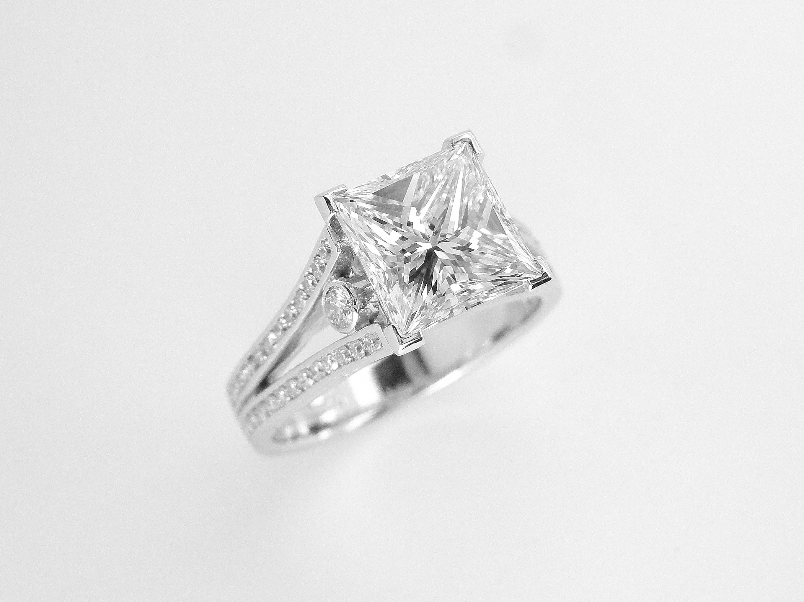 A 2.01ct. 'G' colour Princess cut diamond mounted in a split shoulder platinum ring mount with small round brilliant cut diamonds channel set in shoulders. Ideal diamond size 1.5ct to 5ct