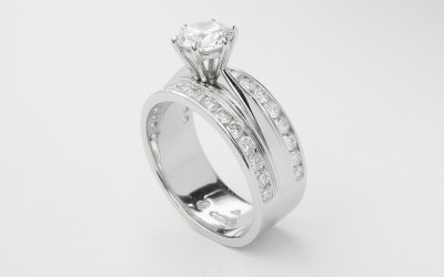 A round brilliant cut 0.91ct. 'F' colour diamond mounted in a broad platinum one piece engagement and wedding ring with round brilliants channel set across the top edges.