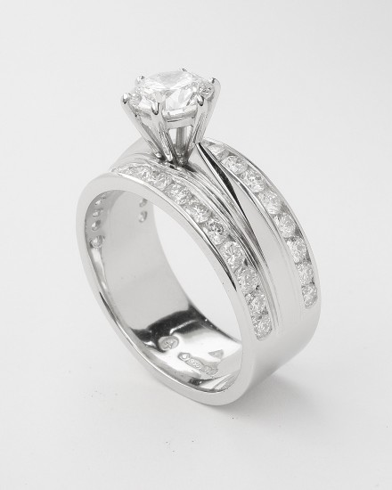 A round brilliant cut 0.91ct. 'F' colour diamond mounted in a broad platinum one piece engagement and wedding ring with round brilliants channel set across the top edges.