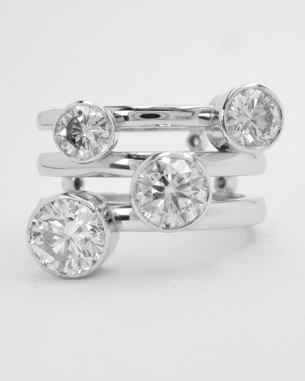 Round brilliant cut diamond 4 stone bezel set (rub-over set) ring with a triple parallel banded ring shank set with small diamonds on reverse side of bands.