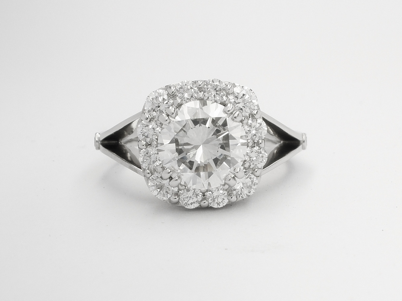 Cushion shaped diamond cluster platinum ring with split shoulder created from 13 round brilliant cut diamonds & diamond set scroll effect round the setting sides. Centre stone 1.90ct 'G' colour.