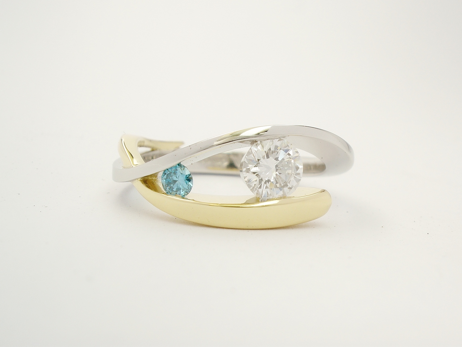 Platinum & 18ct. yellow gold open cross-over 2 stone white & sky blue round brilliant cut diamond ring. Ideal main diamond sizes from 0.35cts. to 0.60cts. & sky blue diamond in proportion.