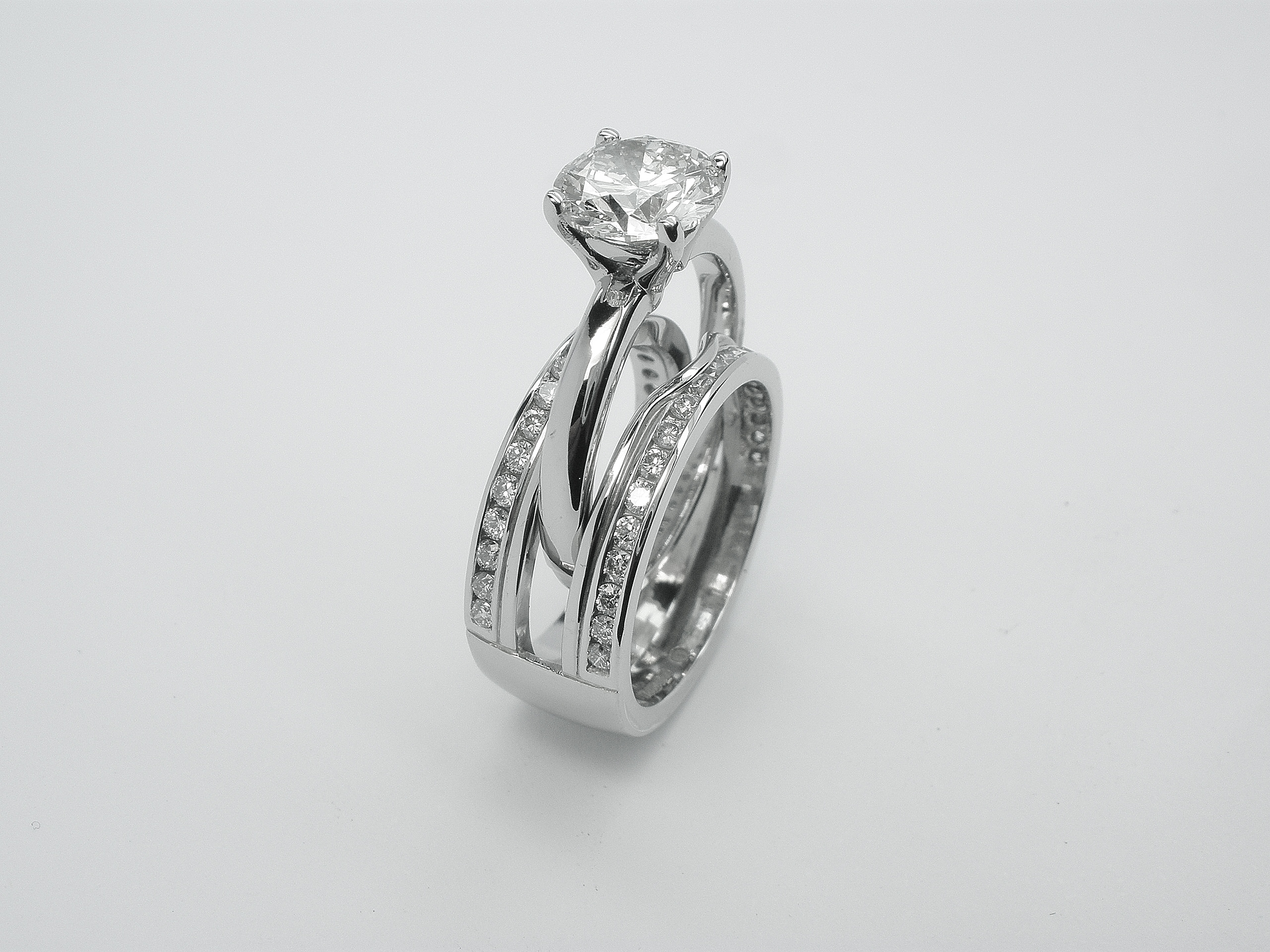 Double 'Embrace' platinum wedding ring channel set with round brilliant diamonds & created to receive the insertion of a single stone round diamond engagement ring.