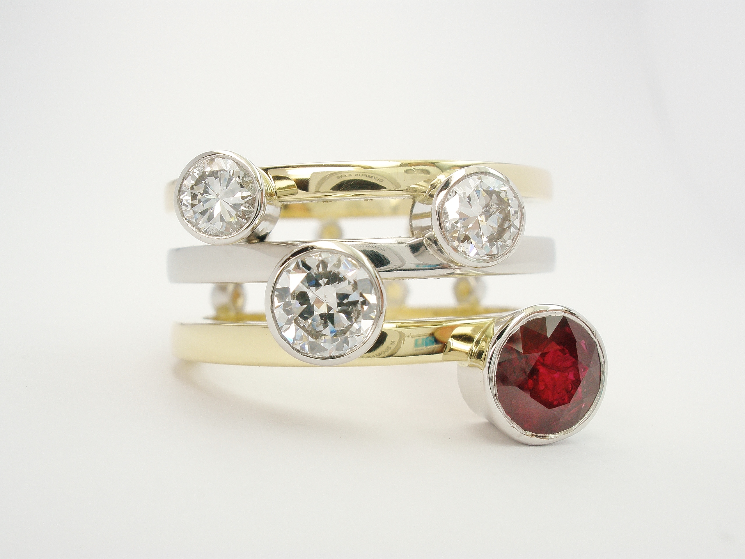 Round ruby & diamond 4 stone platinum rub-over set right handed ring with a triple paralell 18ct yellow gold & platinum banded ring shank set with small diamonds on reverse side of bands.