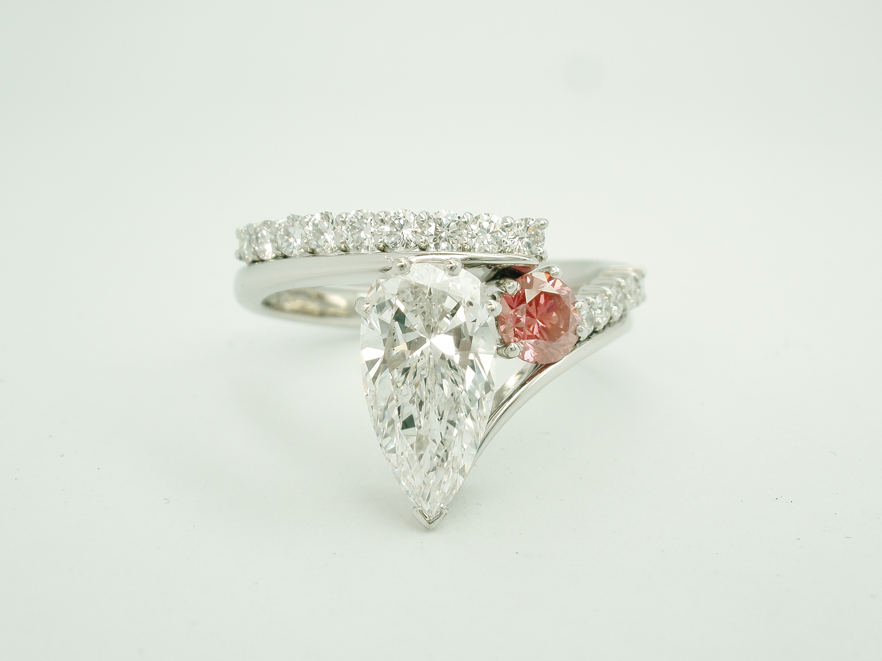 Pink round brilliant cut diamond & white diamond wire set platinum wedding ring shaped to interlock with a single diamond pear wishbone cross-over engagement ring.