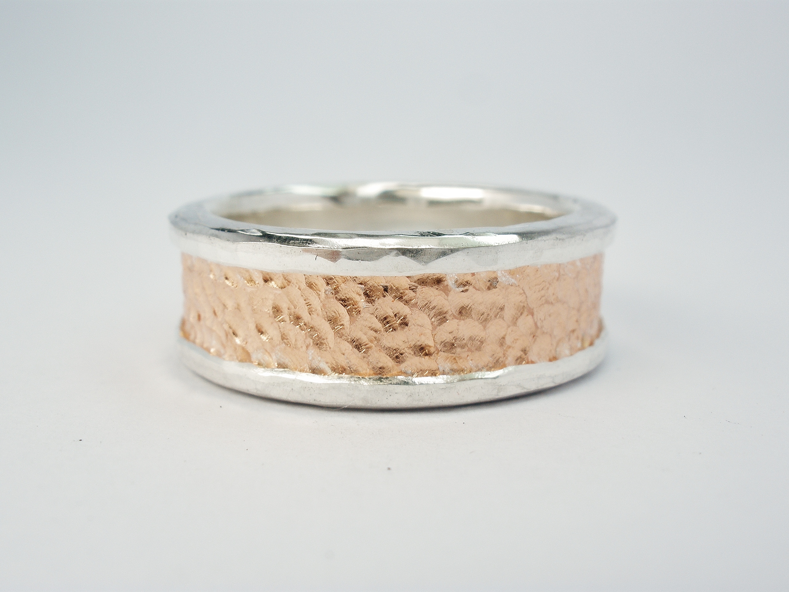 9ct rose gold (also known as red gold or pink gold) & palladium hammer finished gents wedding ring. The centre rose gold a rough texture, the wrap-over palladium edges polished.