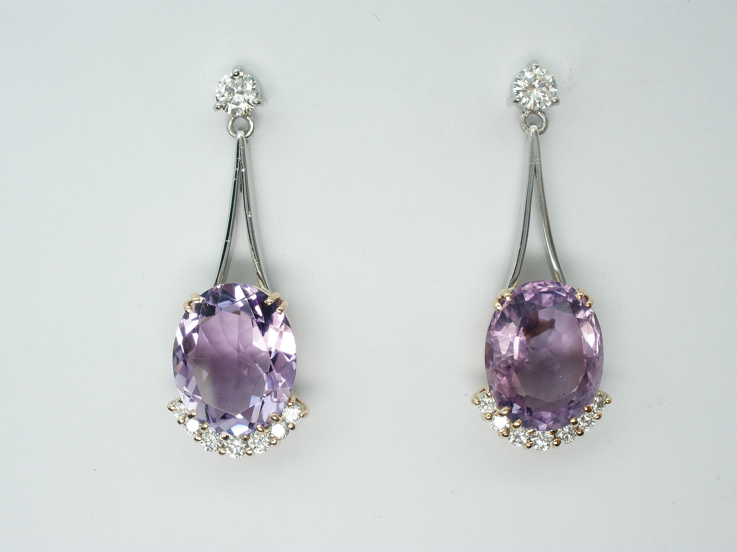 Oval amethyst and round brilliant cut diamond wishbone split wire pendulum style drop earrings.