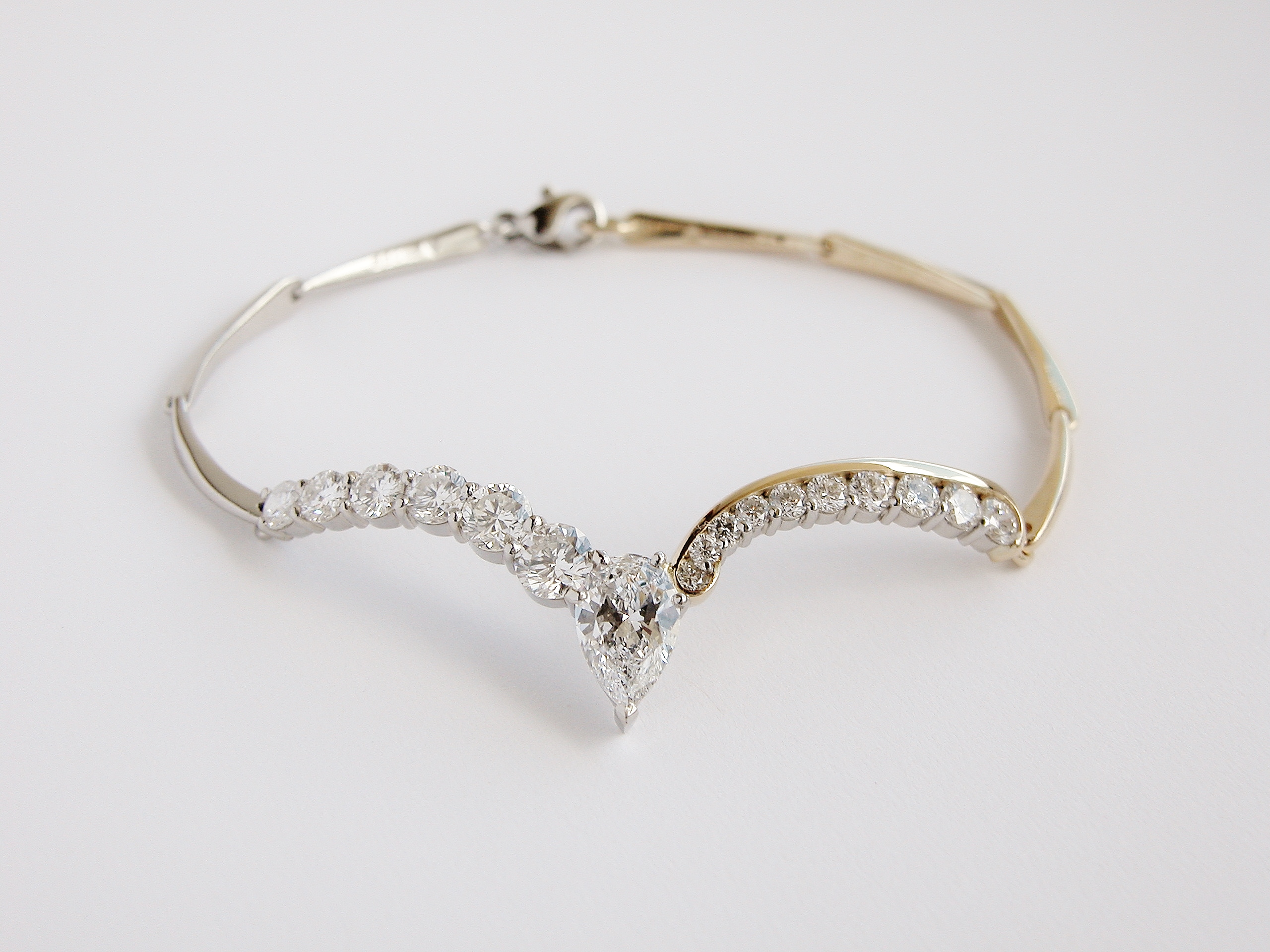 Platinum & 18ct. yellow gold diamond set bracelet with accentual wishbone panel set with a single Pear shaped diamond and 16 round brilliant cut diamonds.