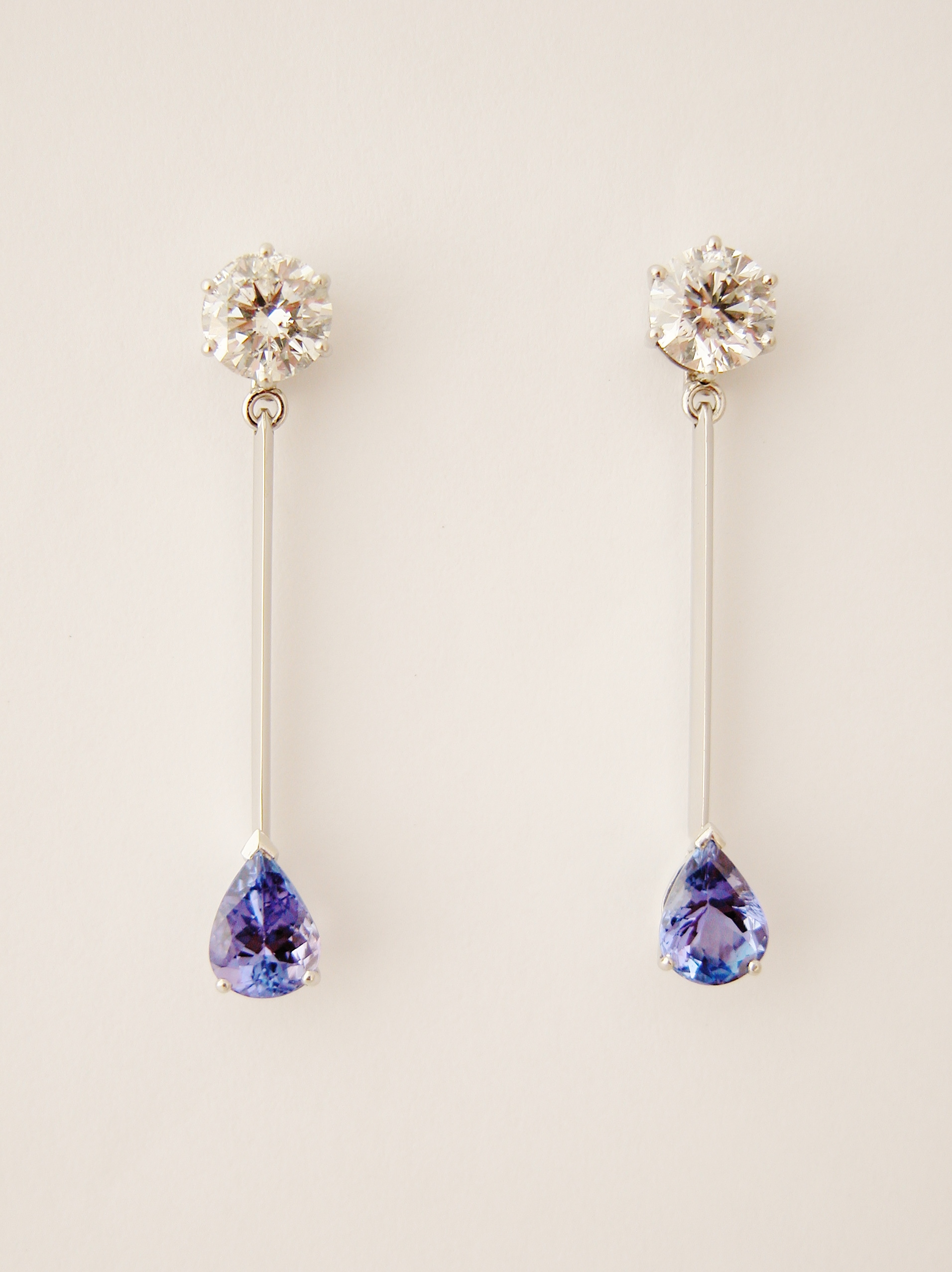 Pair of round brilliant cut Diamond stud earrings with a single pear shaped Tanzanite set at the bottom of a fine wire giving a pendulum effect.