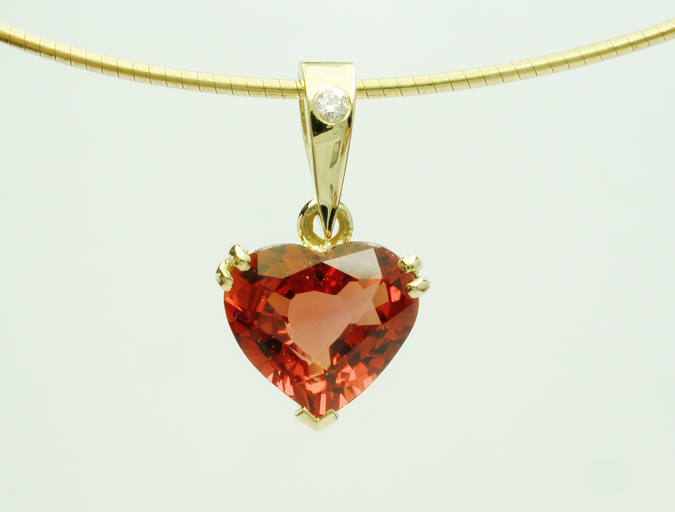 Orange sapphire heart pendant set in 18ct. yellow gold with a diamond set shackle.