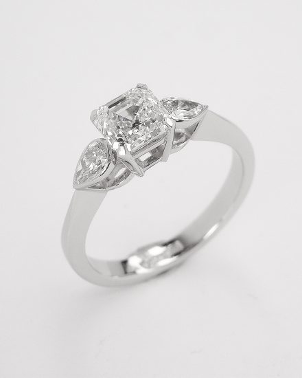 A single 0.82ct. 'E' colour, VS clarity Asscher cut diamond accompanied by a rub-over set pear shaped diamond on each shoulder of the platinum.