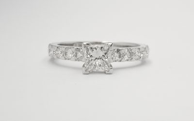 A single princess cut diamond ring mounted in platinum with cut-down set round brilliant cut diamonds in the shoulders.