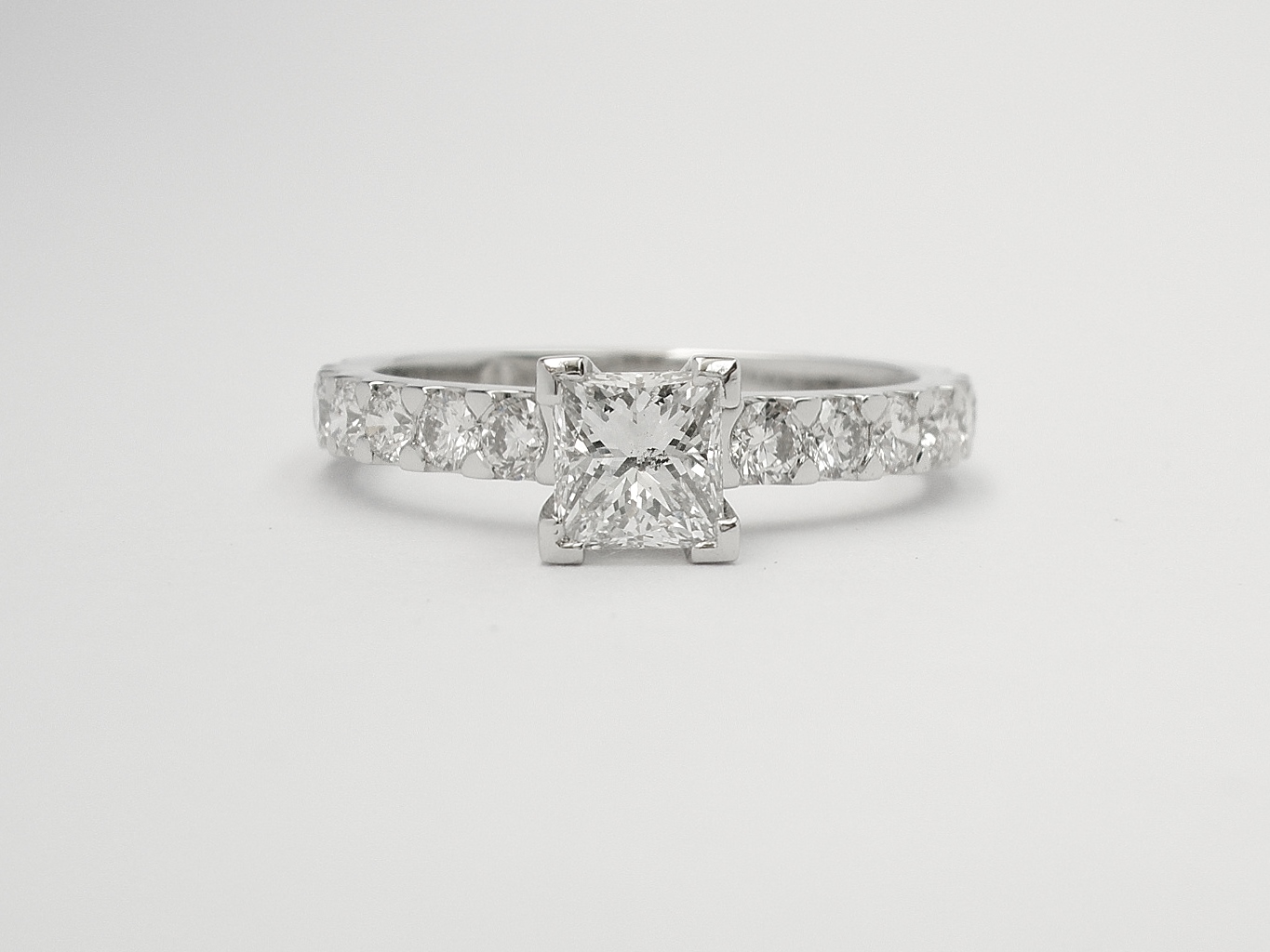 A single princess cut diamond ring mounted in platinum with cut-down set round brilliant cut diamonds in the shoulders.