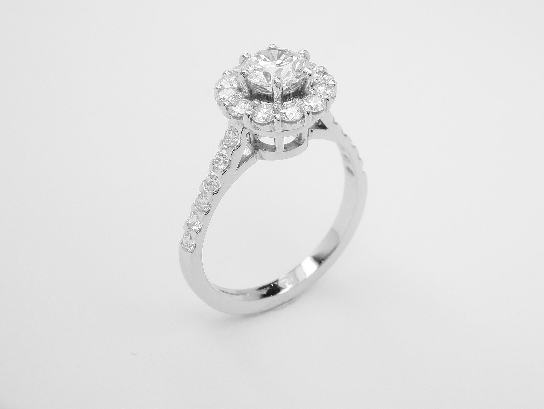 A halo cluster ring comprising of 13 round modern brilliant cut diamonds set in platinum with diamonds cut down set in the shoulders.