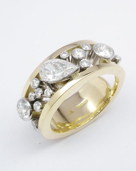 An 18 stone rub-over set pear shaped diamond and round brilliant cut diamond ring mounted in platinum & 18ct. yellow gold.