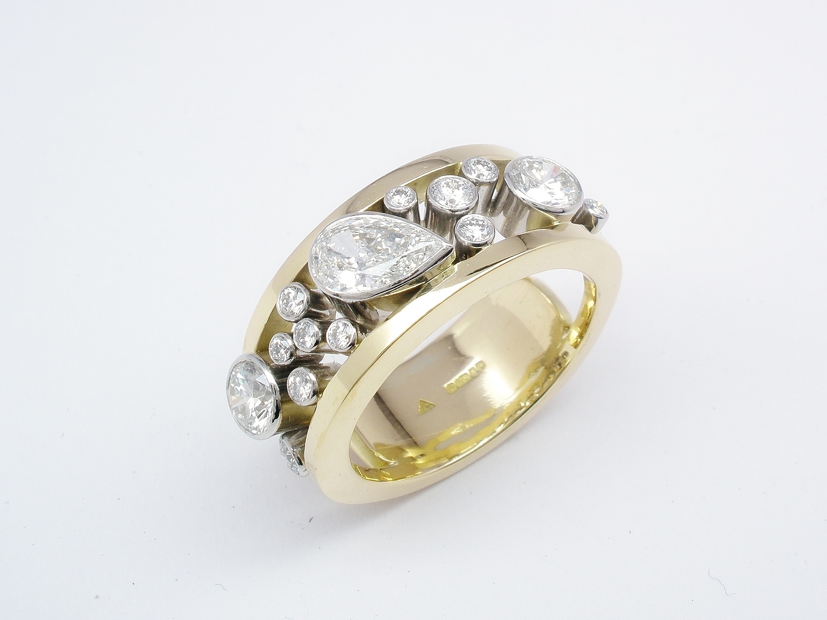 An 18 stone rub-over set pear shaped diamond and round brilliant cut diamond ring mounted in platinum & 18ct. yellow gold.