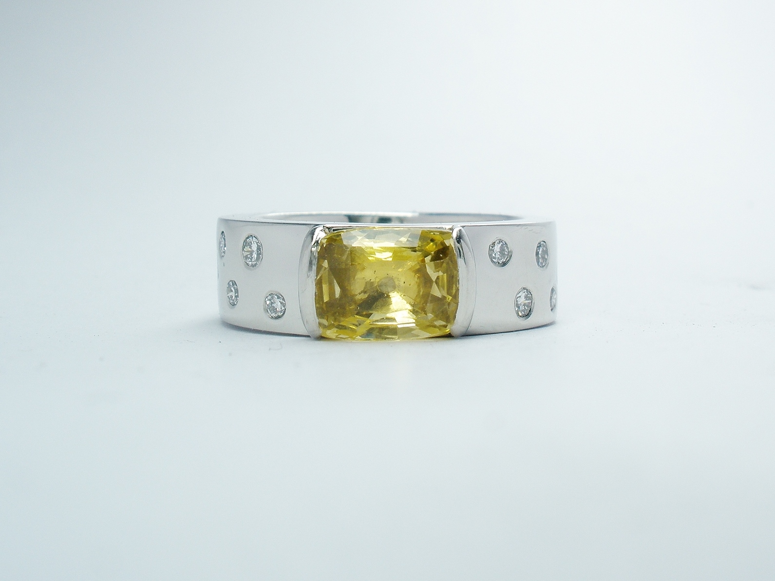 A rectangular cushion cut yellow sapphire and flush set round brilliant cut diamonds mounted in platinum.