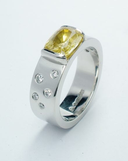 A rectangular cushion cut yellow sapphire and flush set round brilliant cut diamonds mounted in platinum.