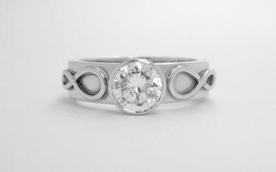 Single rub-over set round brilliant cut diamond ring mounted in platinum with Celtic motif overlay on shoulders.