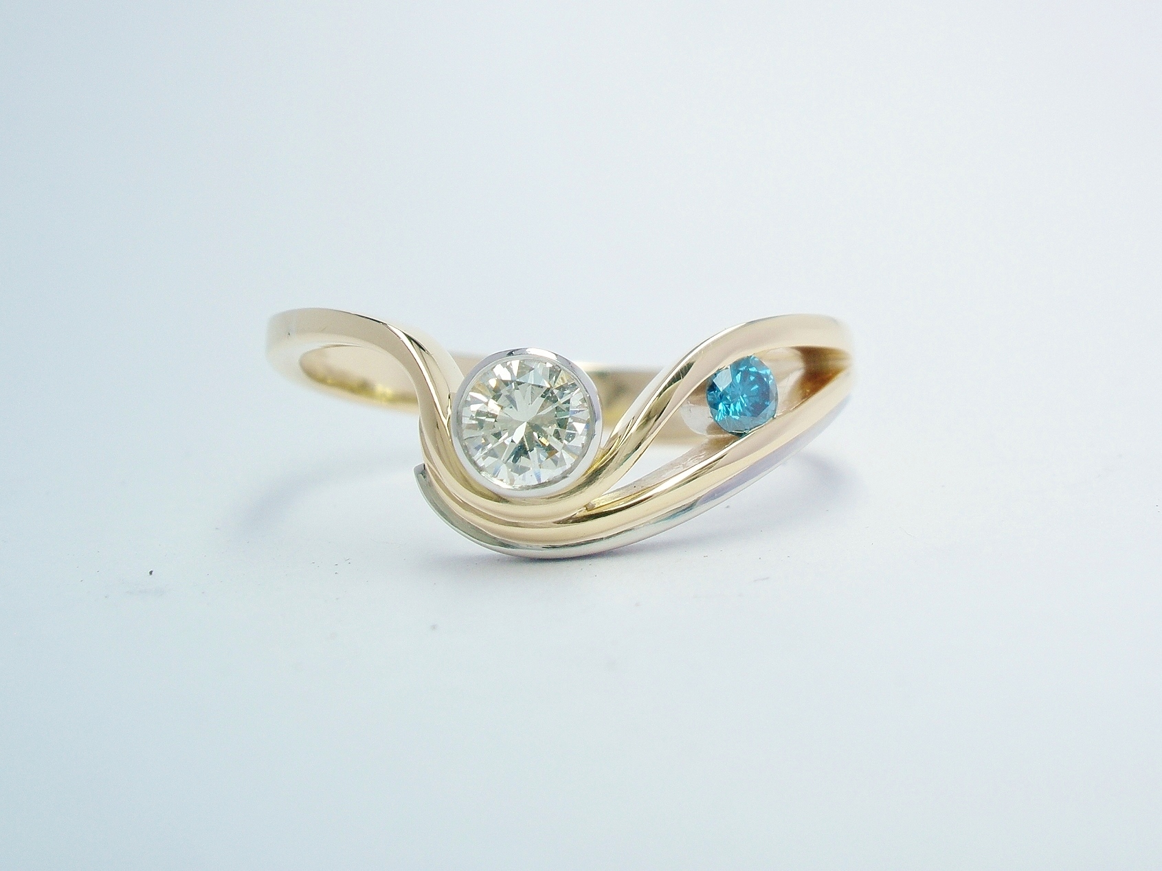 An ocean blue and white 2 stone round brilliant cut diamond 'wave' style ring mounted in 18ct. yellow gold and platinum.