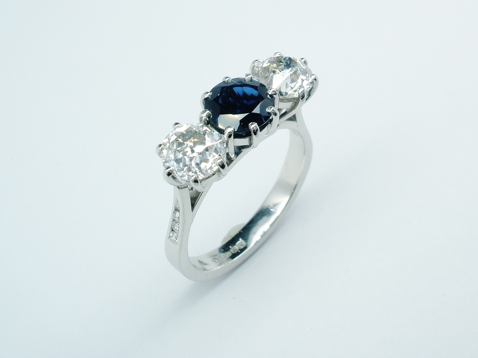 3 stone sapphire & diamond peg set ring mounted in platinum with small diamond channel set in the shoulders.