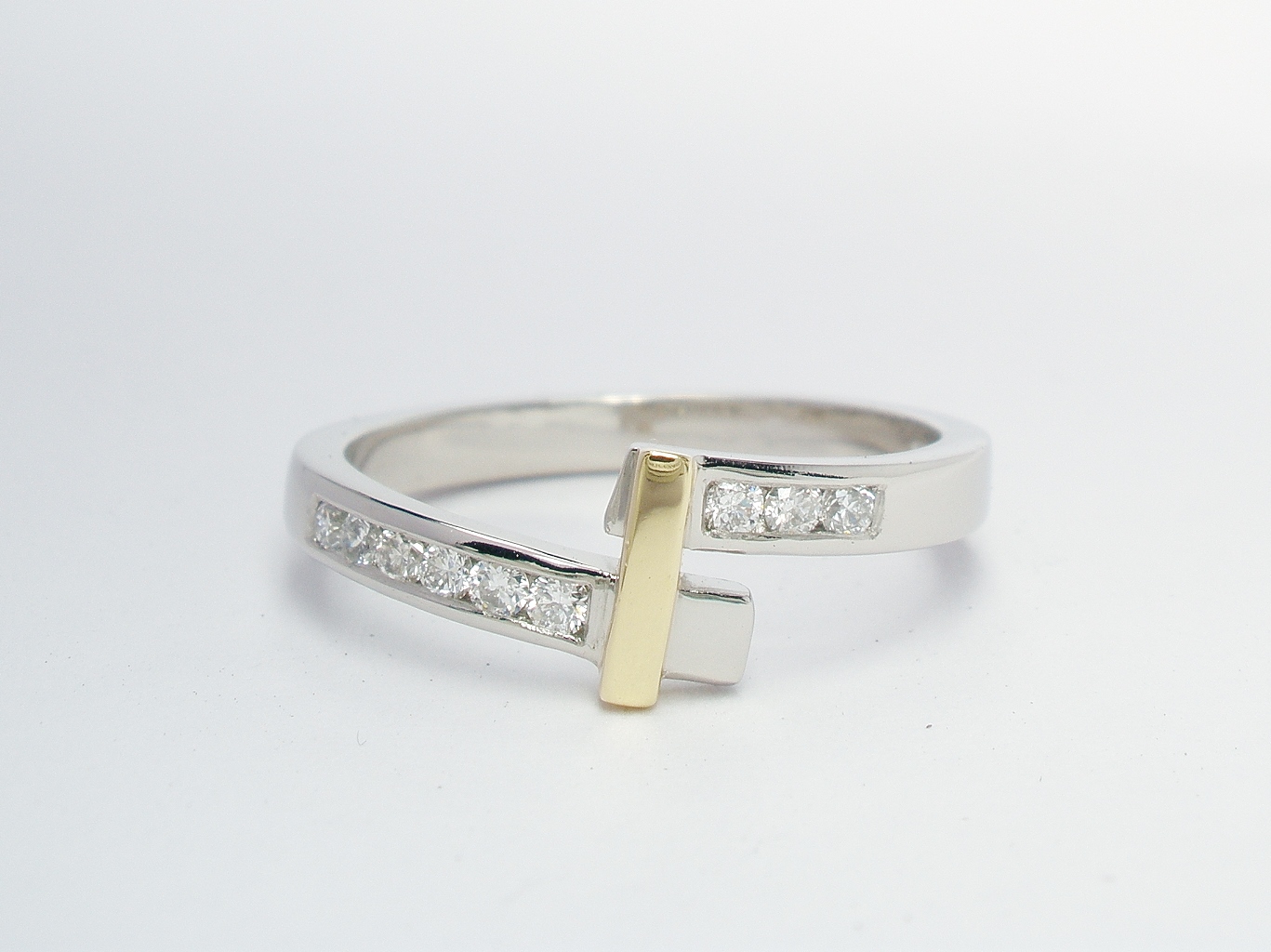 A palladium wedding ring shaped to fit a single stone cross-over diamond ring channel set with diamonds and an 18ct. yellow gold bridge.