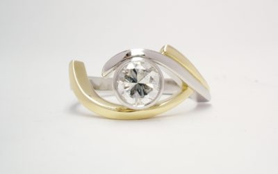 A single stone rub-over set round brilliant cut diamond 'open cross-over' ring mounted in platinum and 18ct yellow gold.