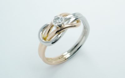 A rub-over set single stone round brilliant cut diamond 'Reef knot' style ring mounted in platinum & 18ct. red gold.