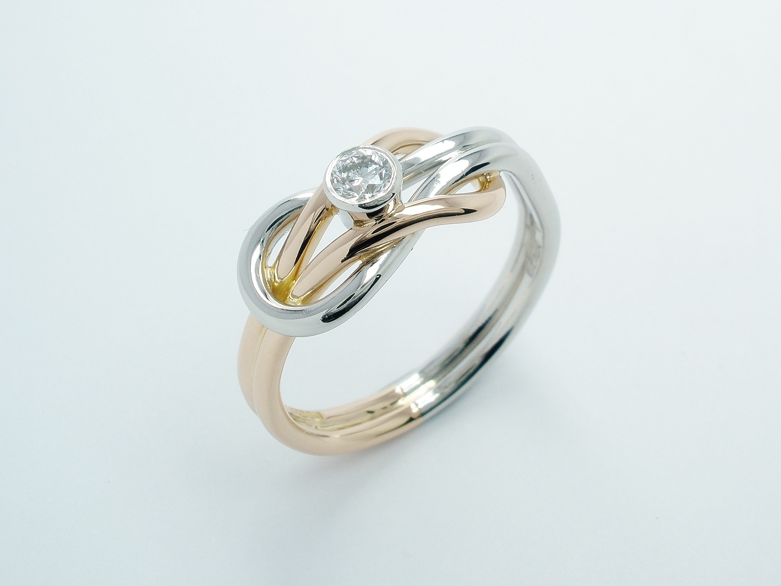 A rub-over set single stone round brilliant cut diamond 'Reef knot' style ring mounted in platinum & 18ct. red gold.