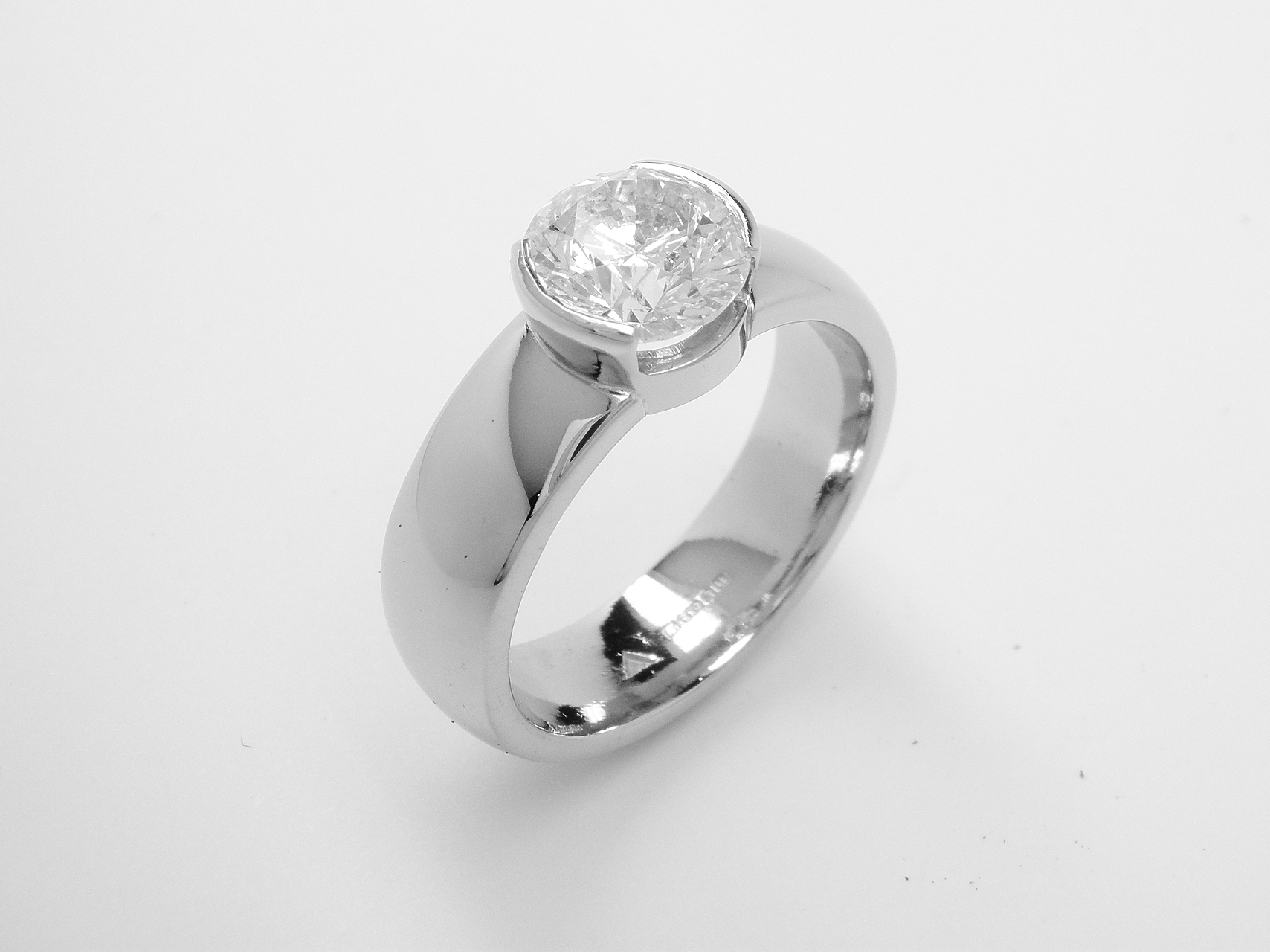 A part rub-over set single stone round brilliant cut diamond ring mounted in palladium and platinum.