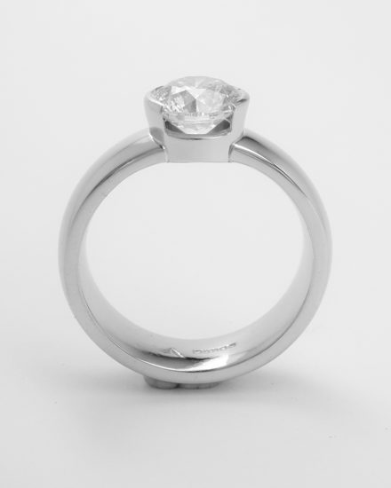 A part rub-over set single stone round brilliant cut diamond ring mounted in palladium and platinum.