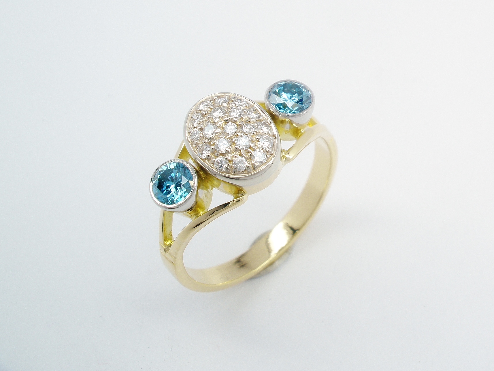 The oval cluster turned to go up the finger and flanked on either side with an HT-HP treated sky blue diamond rub over set in a platinum topped setting.
