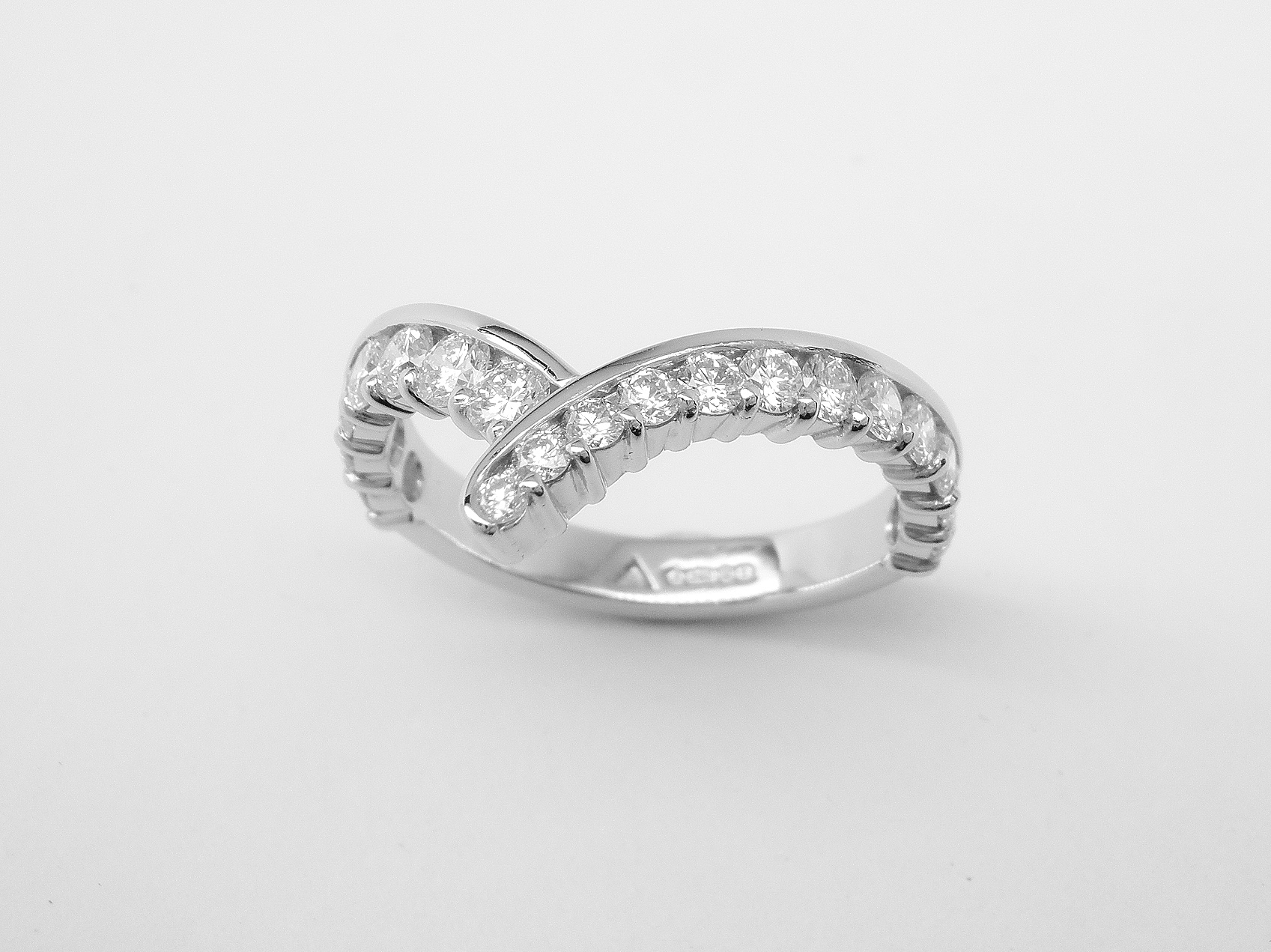 A 19 stone part channel set wishbone cross-over styled ring mounted in platinum. There are 12 tapering diamonds on the right side and 7 of the same size on the left side.