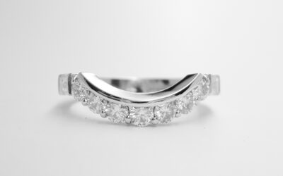 A 9 stone round brilliant cut and baguette cut diamond wedding ring mounted in platinum and shaped to fit around an oval emerald and half moon diamond ring.