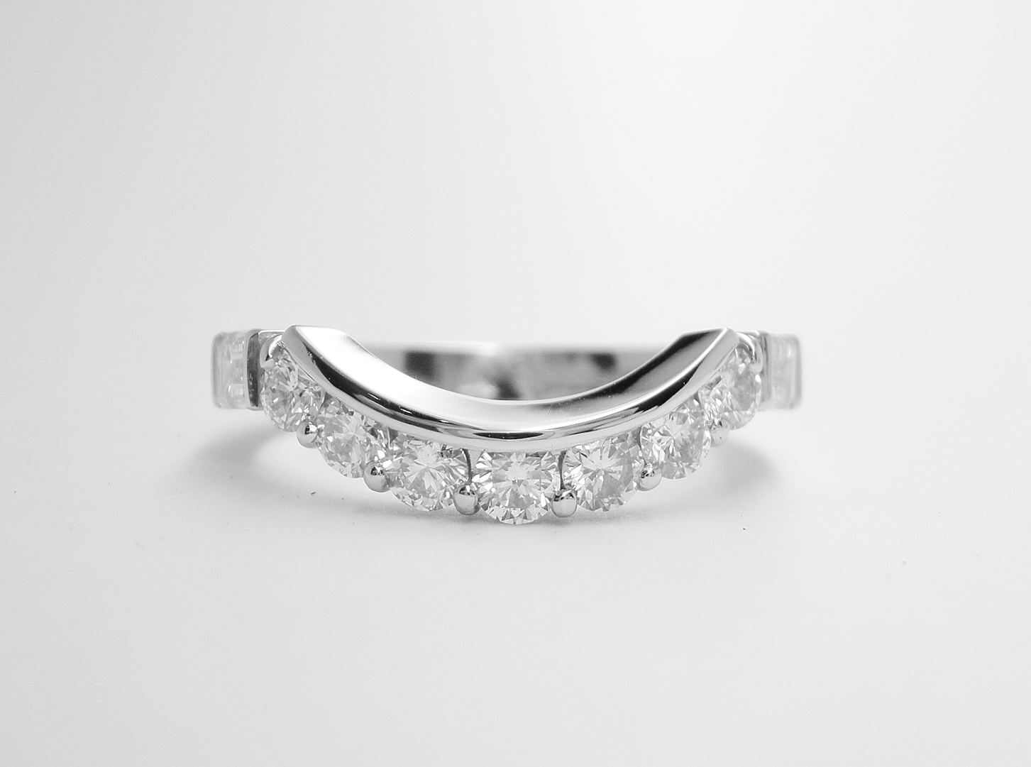 A 9 stone round brilliant cut and baguette cut diamond wedding ring mounted in platinum and shaped to fit around an oval emerald and half moon diamond ring.