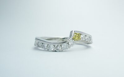 A platinum 11 stone canary yellow & white round brilliant cut diamond part channel set ring shaped to fit around a single stone diamond cross-over ring.
