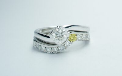 A platinum 11 stone canary yellow & white round brilliant cut diamond part channel set ring shaped to fit around a single stone diamond cross-over ring.