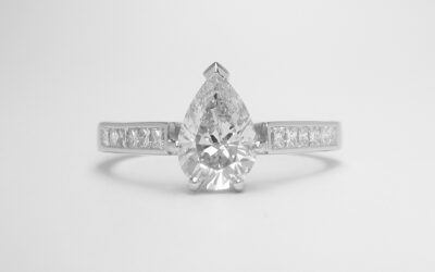 A single stone pear shaped diamond engagement ring mounted in platinum with 6 princess cut diamonds channel set in each shoulder.