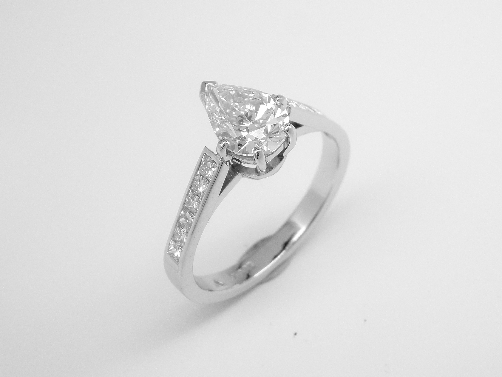 A single stone pear shaped diamond engagement ring mounted in platinum with 6 princess cut diamonds channel set in each shoulder.