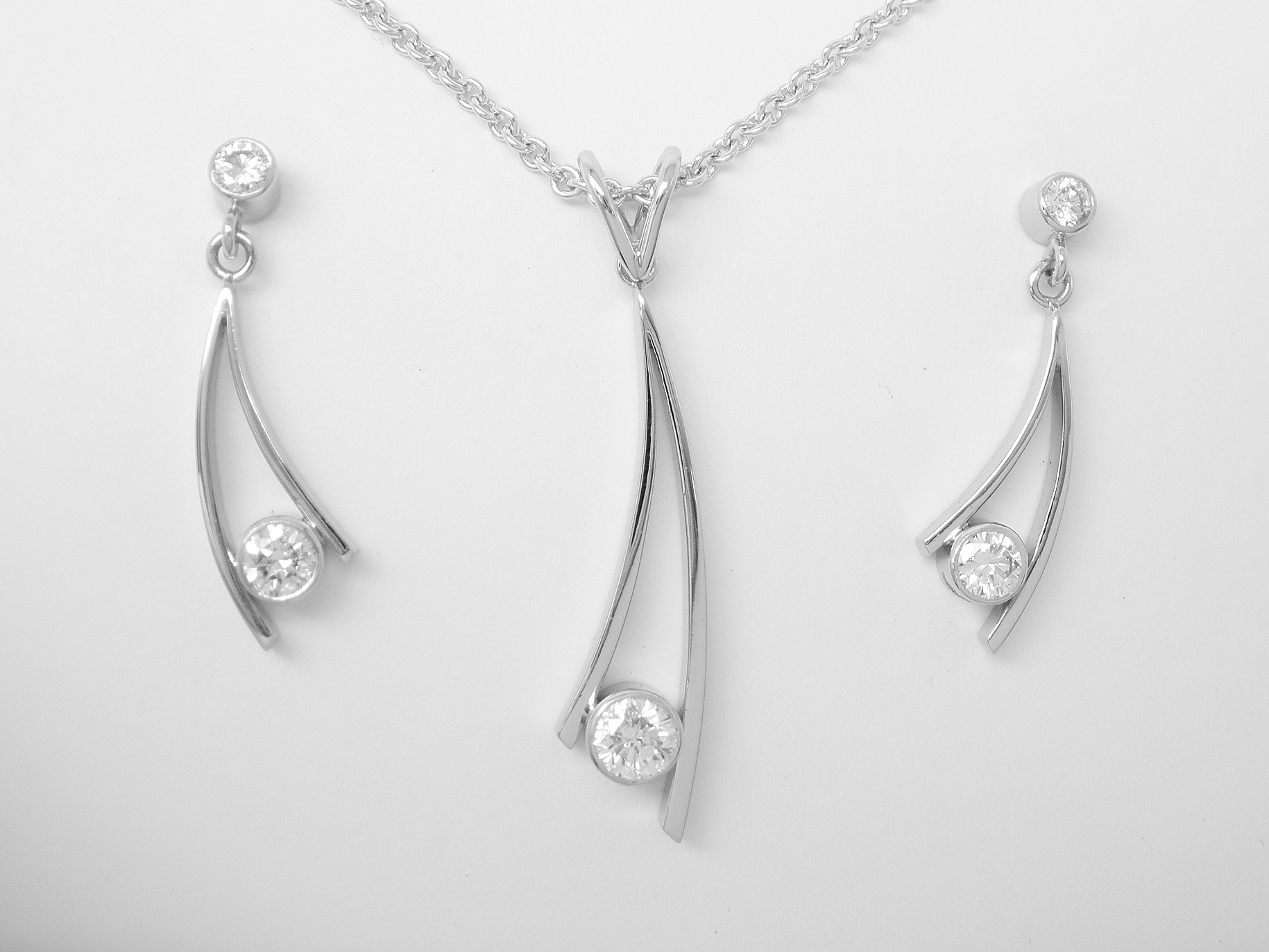 Single stone rub-over set round brilliant cut diamond curved wishbone style pendant & earring set mounted in platinum.