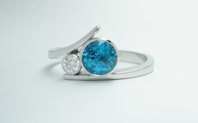A platinum 2 stone rub-over set round blue Zircon and brilliant cut diamond straight wishbone cross-over dress ring.