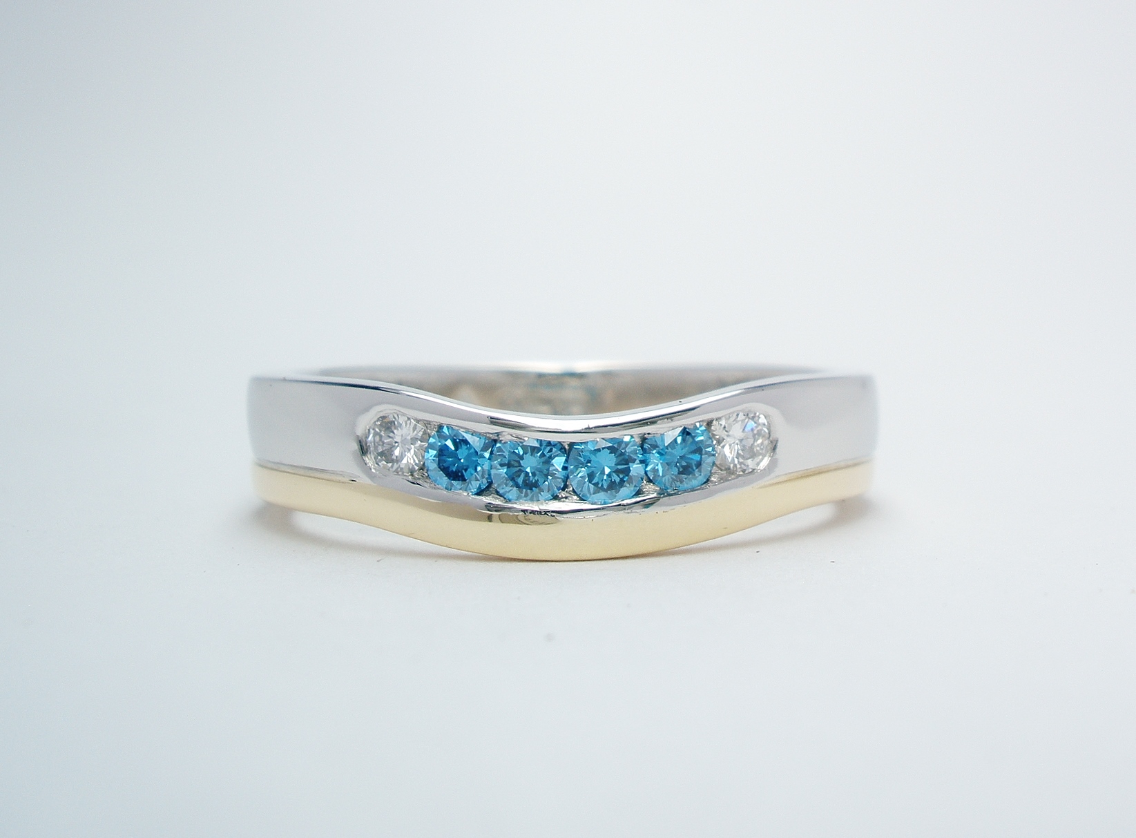 A platinum and 18ct. yellow gold wedding ring shaped to fit around a 3 stone diamond engagement ring and channel set with 4 sky blue & 2 white round brilliant cut diamonds.