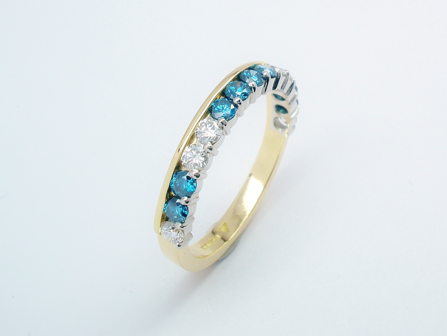 A 14 stone sky blue and white round brilliant cut part channel set ring mounted in 18ct. yellow gold and platinum.