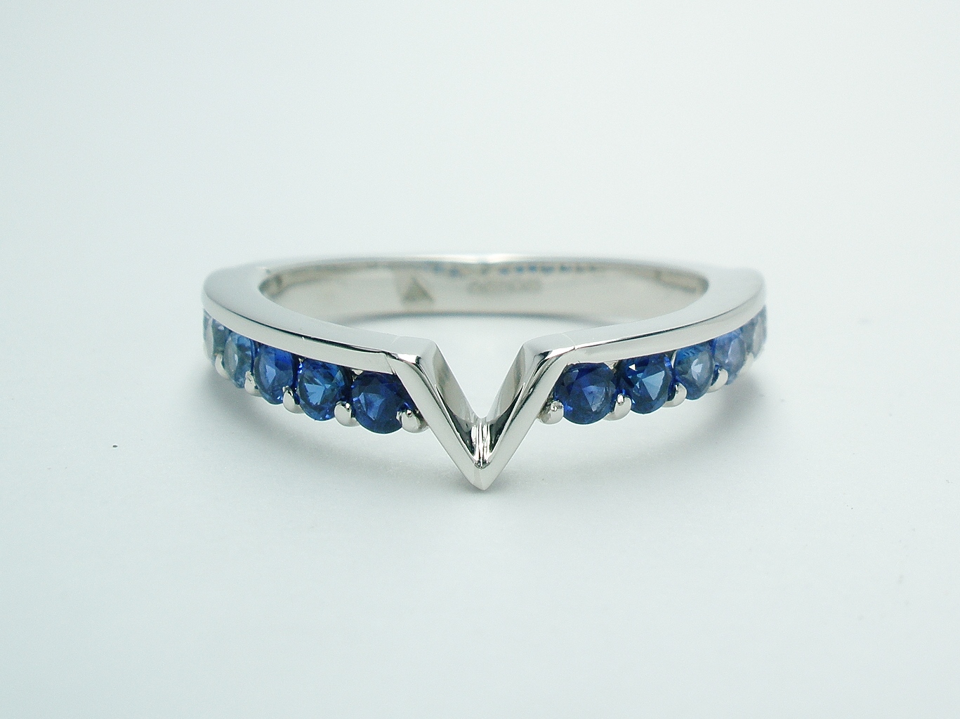 A platinum 14 stone round diamond cut sapphire and diamond part channel set ring shaped to fit around a marquise diamond and trillian cut 3 stone engagement ring.