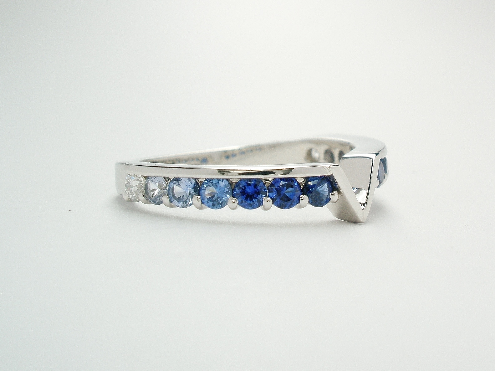 A platinum 14 stone round diamond cut sapphire and diamond part channel set ring shaped to fit around a marquise diamond and trillian cut 3 stone engagement ring.