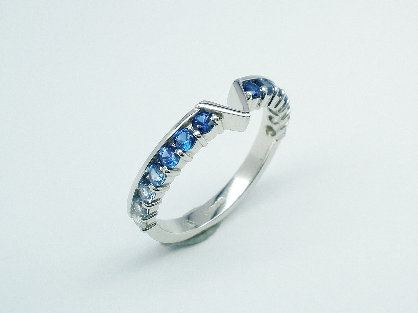 A platinum 14 stone round diamond cut sapphire and diamond part channel set ring shaped to fit around a marquise diamond and trillian cut 3 stone engagement ring.