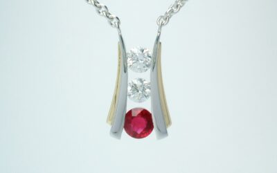 A 3 stone round ruby and round brilliant cut diamond pendant channel set in platinum and trimmed with 18ct. yellow gold.