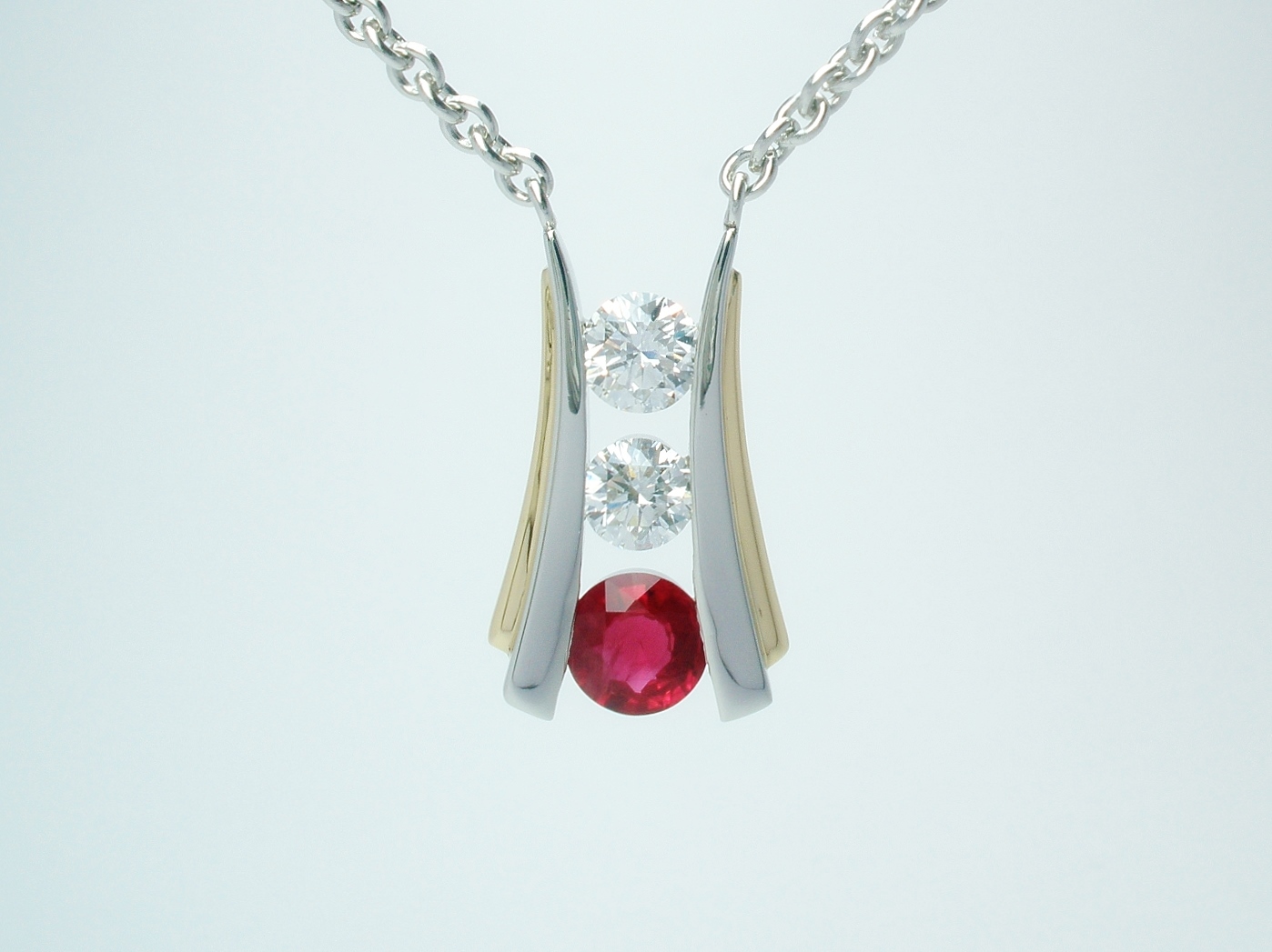 A 3 stone round ruby and round brilliant cut diamond pendant channel set in platinum and trimmed with 18ct. yellow gold.