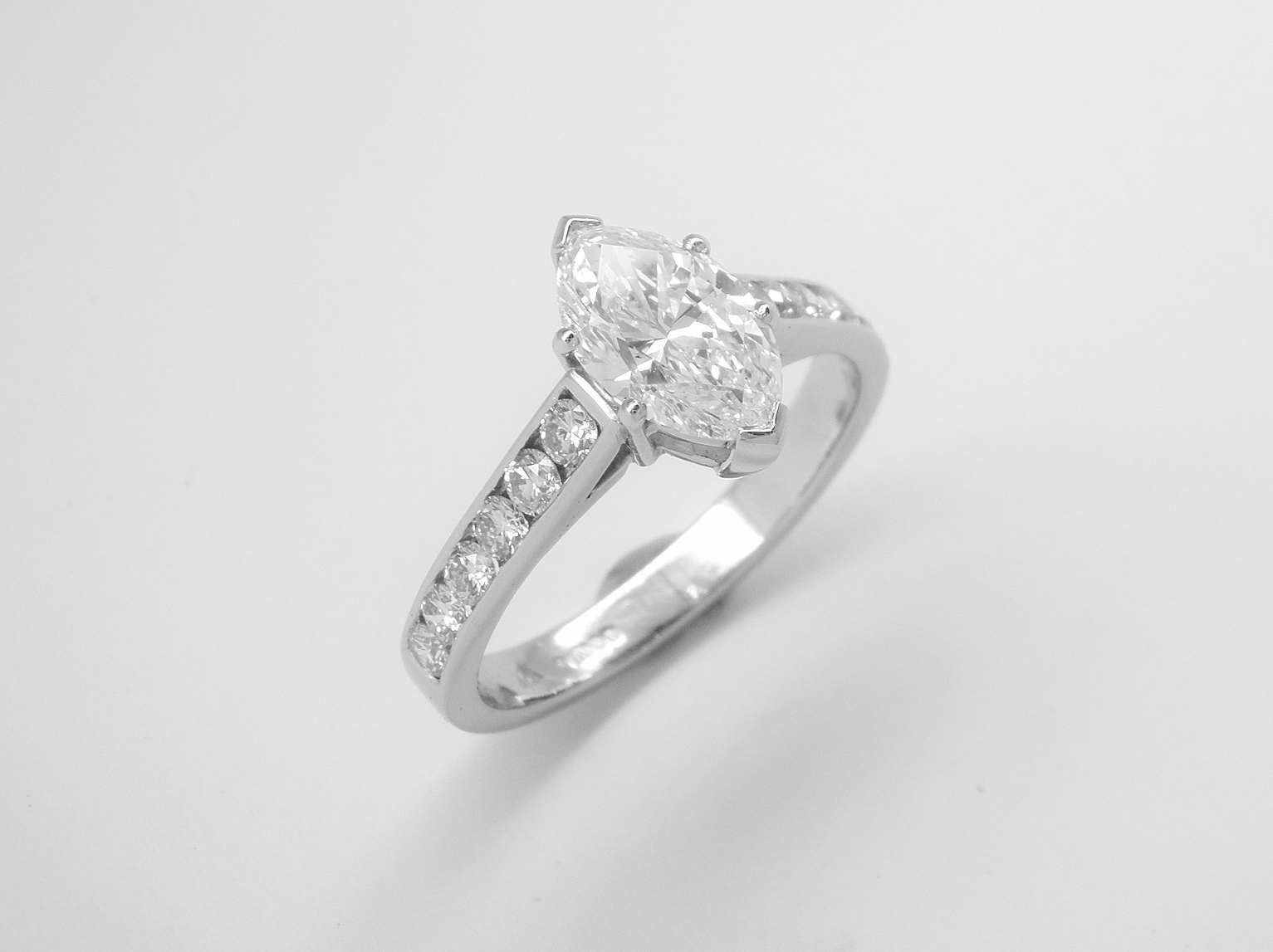A single stone marquise diamond ring mounted in platinum with 6 round brilliant cut diamonds channel set into each shoulder.