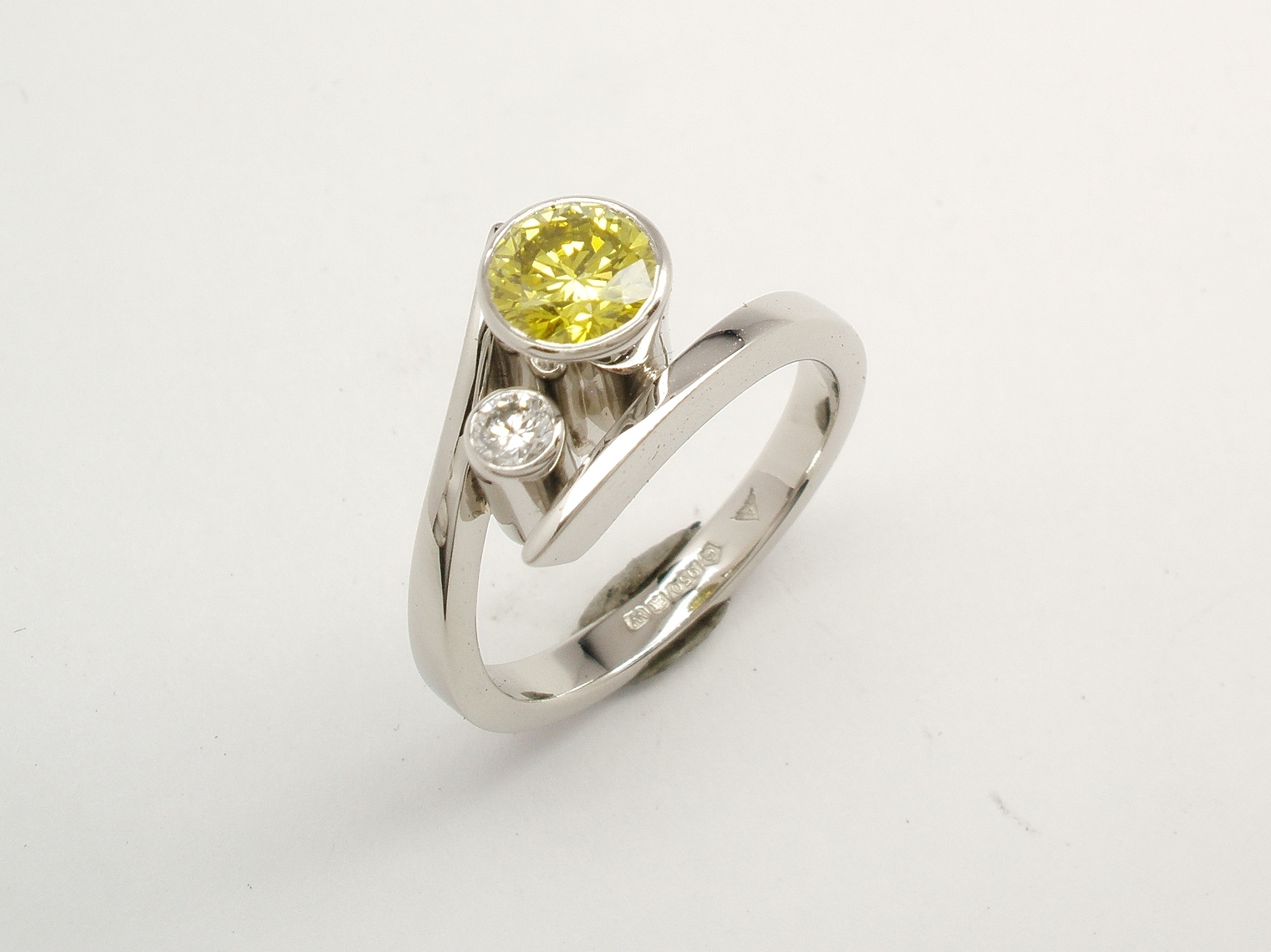 A 2 stone HPHT treated canary yellow and white round brilliant cut straight wishbone cross-over diamond ring. Mounted in platinum.